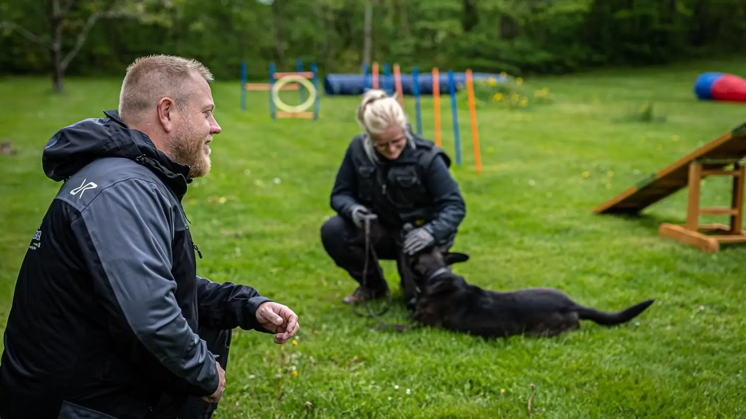 Hundetræner og hundeejer træner sammen med hunden i parken