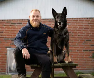 Mand sidder ved hund foran murstensvæg